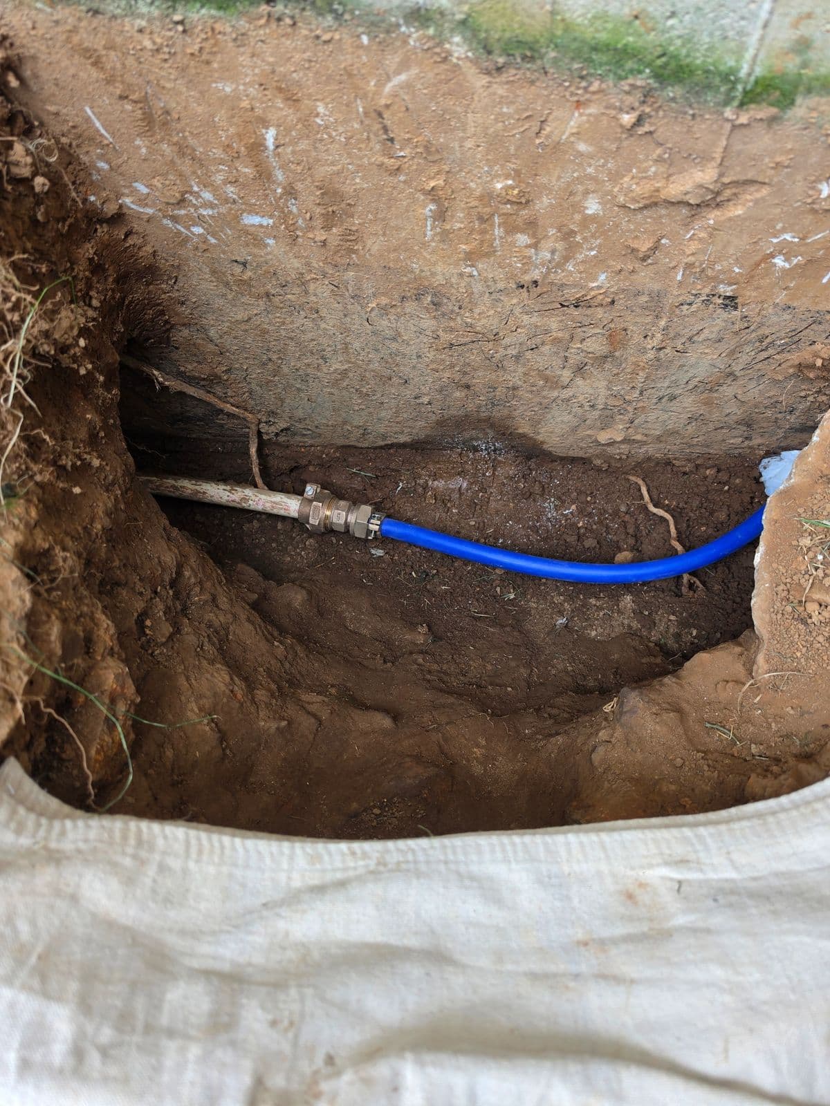 Underground water line connection with brass fitting and PEX in an excavated trench